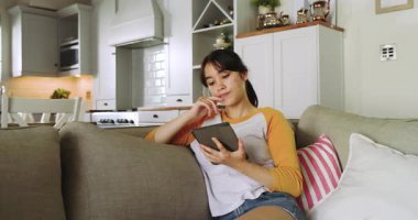 Mutfak bölgesindeki kanepede oturmak, Asyalı bir kadın tableti kapmak, içeriği okumak, uzayı kopyalamak. Günlük, rahatlama, dijital, modern, yaşam tarzı, konfor, iç mekan
