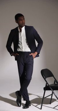 Dikey video: Takım elbiseli adam stüdyoda poz veriyor, modern moda tarzı sergiliyor. Erkek giyim, özgüven, model