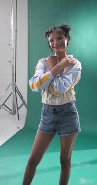 Dikey video: Fotoğraf stüdyosunda kot şortla poz veren kendinden emin genç bir kadın. Portre, moda, güven, modellik, gündelik, moda