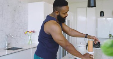 Afro-Amerikalı bir adam modern mutfakta meyve suyu şişesini inceliyor. Tahtayı limonla kesiyor. Meyve suyu, smoothie, mutfak, sağlıklı, hazırlık, taze, modern