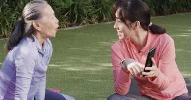 Üst düzey Çinli anne ve kız akıllı olanları kontrol ediyor, açık havada telefon izliyor şişeden içiyor. Aile, spor, açık hava aktivitesi, bağlılık, sağlık, rahatlık, arkadaşlık.