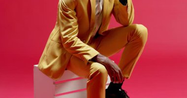 Hardal takım elbiseli alt yarı Afro-Amerikalı adam pembeleşmiş arka planda ceketini düzeltiyor. Moda, zarafet, güven, profesyonellik, tarz, portre, iç mekan