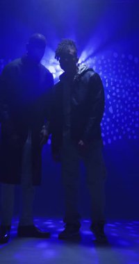 Dikey video: Enerjik bir şekilde dans eden, soluk mavi ışık efektli Afrikalı Amerikalı erkekler stüdyoda. Dans, koreografi, hareket, karamsar ışıklandırma, erkek, performans
