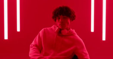 Kırmızı neonun altında sandalyeye oturan, stüdyoda oturan, kulaklıkları tutan, iç ritmi tutturan bir adam. Stüdyo, eğlence, neon, ruh hali, konsantrasyon, performans, iç mekan