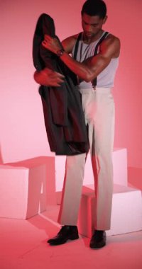 Dikey video: Pantolon askısı giymiş şık bir adam ceketini ayarlıyor, stüdyoda güven içinde poz veriyor. Moda, tarz, güven, erkek giyim, portre, giysi