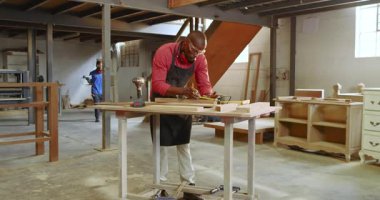 Afrika kökenli Amerikalı erkek marangoz atölyede yeni çerçeve hizasını inceliyor. El işi, ahşap işçiliği, inşaat, sanayi, atölye, hassasiyet, takım çalışması