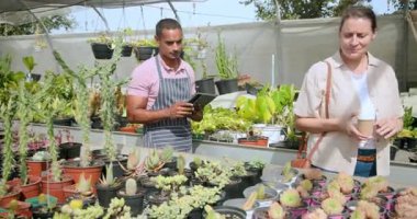 Bahçe uzmanı, bitki detaylarını tabletten seradaki müşteriye gösteriyor. Bahçecilik, danışmanlık, botanikçi, teknoloji, etkileşim, perakende