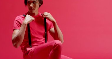 Sandık kenarları sürükleyici, Asyalı bir adam diz çöküyor, pantolon askılarını ayarlıyor ve kırmızı stüdyoda dans ediyor. Dinamik, minimalist, hareketli, atletik, modern, performanslı, enerjik