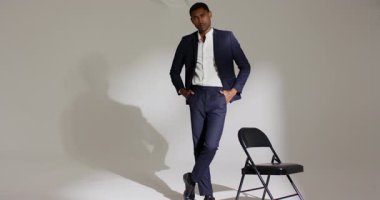 Stüdyoda Afrikalı Amerikalı bir adam sandalyeye yaslanıyor, yakasını düzeltiyor, poz veriyor. Profesyonel, kendinden emin, moda, zarafet, poz, tarz, girişimci