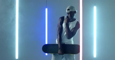 Neon Stüdyosu 'nda tekerlekleri kontrol etmek için tahtayı kaldıran Afrikalı Amerikalı adam. Kentsel, sokak kıyafetleri, dinamik, modern, genç, atletik, yaratıcı