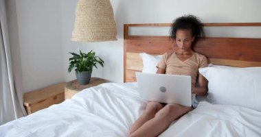 Evde dizüstü bilgisayar kullanan gülümseyen bir kadın, rahat çalışma ortamının tadını çıkarıyor. Uzaktan çalışma, ev ofisi, teknoloji, serbest çalışma, rahatlama, rahatlama