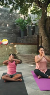 Dikey video: Anne ve kızı dışarıda minderlerde yoga yapıyor, barışçıl meditasyonun tadını çıkarıyorlar. Sağlık, aile, rahatlama, uyum, farkındalık, bağ.