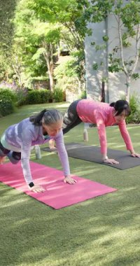 Dikey video: Bahçedeki minderlerde yoga yapan iki kadın, birlikte açık havada egzersiz yapmaktan zevk alıyorlar. Sağlık, fitness, açık hava aktiviteleri, meditasyon, rahatlama