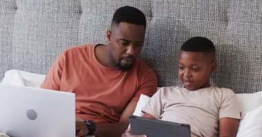 Tablet tap dansı, Afrikalı Amerikalı baba ve oğulun laptoplarını kapatarak kanepede tablet içeriğini keşfetmelerini sağlar. Aile, bağ, eğitim, teknoloji, sade, birliktelik, modern