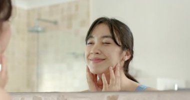 Asyalı bir kadın banyo aynasında yanaklarına nemlendirici sürüyor, perçem ayarlıyor, akıllı bant takıyor. Cilt bakımı, bakım, güzellik, yansıtıcı, sağlık, minimalizm.