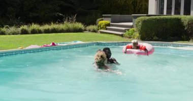 Çeşitli aileler kızlarını pembe tüpten tutuyorlar, havuz başındaki kızı eğlence olsun diye kaldırıyorlar. Aile, eğlence, boş zaman, yaz, eğlence, kaynaşma, kutlama