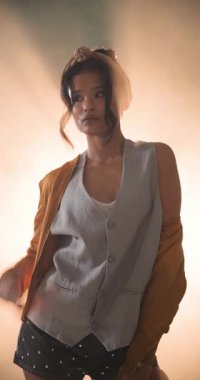 Dikey video: Gündelik grunge kıyafetli genç bir kadın sıcak stüdyo ışıklarıyla rahatça poz veriyor. Moda, tarz, tutum, portre, ifade, moda