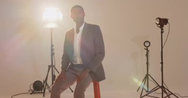 Afrikalı Amerikalı adam kol saatini kontrol etmeden önce stüdyo yumuşak takım elbise yakasında kırmızı taburede duruyor. Profesyonel, portre, stüdyo, ışıklandırma, kıyafet, erkek, sofistike