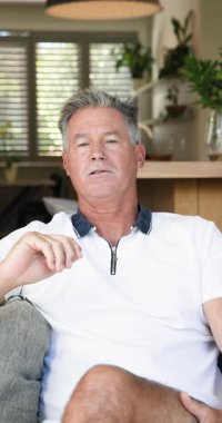 Dikey video: Evde dinlenmek, olgun bir adamın koltukta otururken jest yapması, düşünceli görünmesi. Rahatlama, tefekkür, sükunet, yaşam tarzı, rahatlık, rahatlık