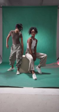 Dikey video: Stüdyoda yeşil zemin ile güvenle poz veren iki şık şahıs. Moda, tarz, giysi, modellik.