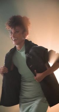 Dikey video: Deri ceketli kendine güvenen bir kadın şık bir stüdyoda poz veriyor. Moda, tarz, trend, şehir, portre, kenar mahalle