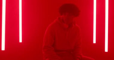 Kırmızı tüplerin aydınlatılması üzerine, adam kaideye tırmanıyor, kulaklıklarla stüdyoya uzanıyor ve yansıyor. Düşünce, yalnızlık, içgözlem, ortam, minimalist, karamsar, fütürist