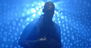 Orta yaşlı Afrikalı Amerikalı bir adam sahne arkasında titreşen ışığa tepki veriyor, adım atıyor ve ceketini ayarlıyor. Siluet, dramatik ışıklandırma, modern, dramatik, karamsar, anlamlı, şık