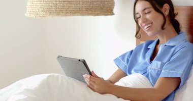 Pijamalı gülümseyen kadın yatakta tablet kullanıyor, evde sabah rahatlığının tadını çıkarıyor. Yaşam tarzı, teknoloji, rahatlık, rahatlık, boş zaman, dijital