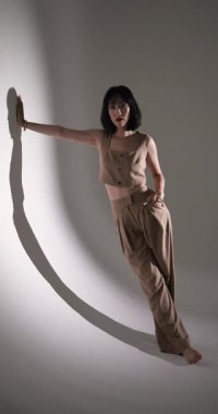 Dikey video: Model stüdyo arkaplanına karşı güvenli bir şekilde bej kıyafetler giyerek poz veriyor. Moda, tarz, modellik, zarafet, moda, giyim