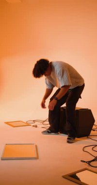 Dikey video: Genç adam stüdyoda hoparlörde oturuyor, kablolar ve ekipmanlarla çevrili. Müzik, kayıt, ses, teknoloji, müzisyen, ses