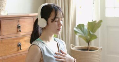 Yetişkin bir Asyalı kadın beyaz kulaklık takıyor ve nefes aldıktan sonra siyah yoga minderini içine çekiyor. Meditasyon, farkındalık, sağlık, rahatlama, iç mekan, huzur, odaklanma