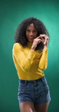 Dikey video: Sarı bluzlu kendine güvenen kadın kıvırcık saçlarını yeşil arka plana ayarlıyor. Moda, saç stili, güzellik, poz, cazibe, yaşam tarzı