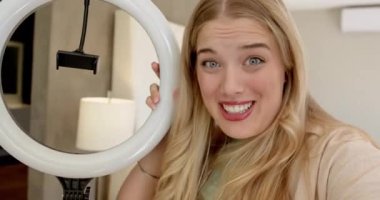 Kadın video kaydedicisi izleyicileri selamlıyor, telefon bağlantısı kaldırılıyor, evde halka ışığı kurulumu gösteriliyor, kopyalama alanı. Stüdyo aydınlatma, içerik yaratma, güzellik, yaşam tarzı, minimalist, teknoloji, etkileyici