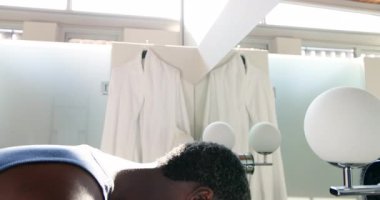 Afro-Amerikalı bir adam aynada güneşli bir banyoda saçını tarıyor, fotokopi çekiyor. Kişisel bakım, bakım, yansıma, sağlık, kişisel alan, aydınlık, iç mekan.