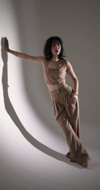 Dikey video: Moda stüdyosunda duvara yaslanmış şık bej kıyafetlerle poz veren model. style, editorial, clothes, trend, photoshoot, dress