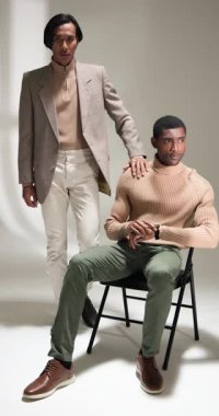 Dikey video: Modern kıyafetler içindeki şık adamlar moda stüdyosunda güven içinde poz veriyorlar. Erkek giyim, tarz, trend, modellik, çağdaş, şık