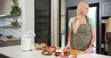 Çeşitli arkadaşlar mutfak adasında gübreleme yapıyor sonra salatada biber öğütüyor ve beşlik çakıyor. Sürdürülebilirlik, işbirliği, tazelik, organik, modern, çevre dostu, mutfak