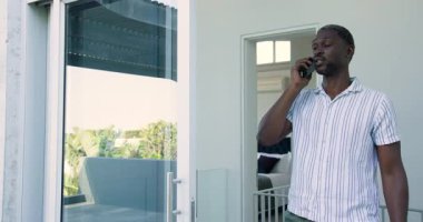 Afro-Amerikalı adam balkonda dikiliyor, akıllı telefonla konuşuyor, açık kapının yanında gülümsüyor. Balkon, yeşillik, iletişim, gündelik, modern, yaşam tarzı, bağlantı