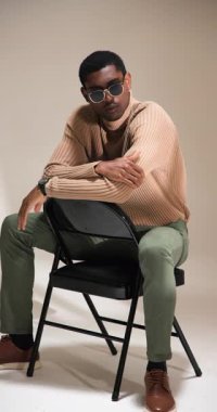 Dikey video: Şık bir süveter ve pantolon giymiş, sandalyede oturan, düşünceli görünen bir model. stil, giysi, moda, tefekkür, gündelik, tarz