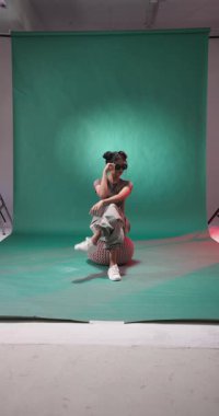 Dikey video: Şık giyinmiş genç bir kadın yaratıcı stüdyo ortamında yerde oturuyor. Moda, yaratıcılık, tarz, sanatsal, tasarım, çağdaş