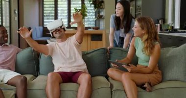 Beyaz adam, VR kulaklığı takmadan hemen önce tablet alıyor. Arkadaşları evde rehberlik ederken el kol hareketi yapıyor. Etkileşimli, teknoloji, eğlence, sosyal, yaşam tarzı, canlı, modern