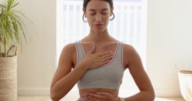 Kadın, elleri göğsünde, gözleri kapalı, evinde huzurlu hissederek farkındalık egzersizi yapıyor. Meditasyon, sükunet, rahatlama, refah, huzur, uyum.