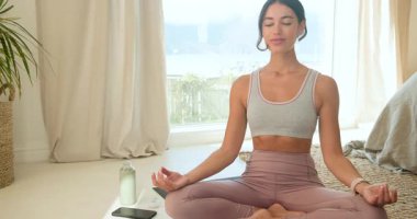 Yoga yapıyor, evde meditasyon yapan bir kadın akıllı telefon ve su şişesiyle yakınlarda. Sağlık, farkındalık, fitness, rahatlama, denge, öz bakım
