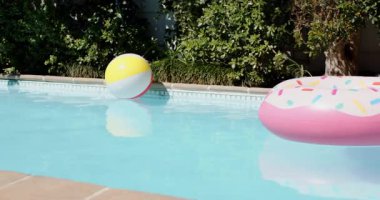 Şişirilebilir plaj topu ve donut, hafif esinti altında güneşli arka bahçedeki havuzda sürükleniyor. Açık hava, boş zaman, rahatlama, dinginlik, canlı, neşeli, su.