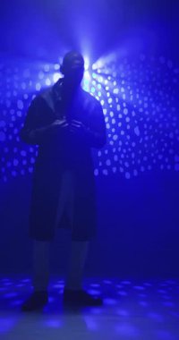 Dikey video: Stüdyoda mavi ışıkların altında dans eden uzun montlu bir adam, dinamik siluet yaratıyor. Dans, hareket, koreografi, gece hayatı, enerjik, performans
