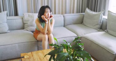 Asyalı kız ve anne, kanepede telefonu kaydırıyor. Annesi seramik bardaklarla içeri giriyor. Rahatlatıcı. Empati, destek, aile, duygusal, konfor, yerli, modern