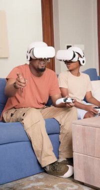 Dikey video: Evde VR kulaklık takan Afrikalı baba ve oğul hedeflere tepki veriyor. Aile, yenilik, sürükleyici, teknoloji, eğlence, bağlantı, dikey video