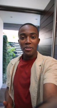 Dikey video: Afro-Amerikalı adam kendini tanıtmak için kapıyı telefonla açıyor. Modern mimari, karşılama, yaşam tarzı, gündelik, iç tasarım, açık alan, dikey video