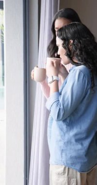 Dikey video: Pencereden bakan kadın bir çift bardaklarını yudumlayarak akıllı bakıyorlar. Rahatlama, arkadaşlık, samimiyet, samimiyet, dostluk, huzur, dikey video