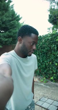 Vertical video: Stepping into patio raising smartphone, African American man rehearsing speech. Outdoor, lifestyle, candid, leisure, natural, authenticity, vertical video